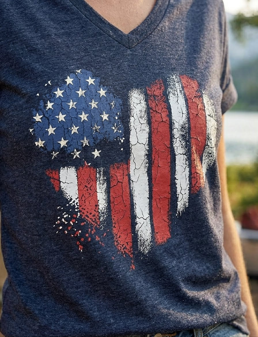 A close-up of a person wearing a heather navy blue V-neck t-shirt with a distressed, cracked American flag graphic on the front.