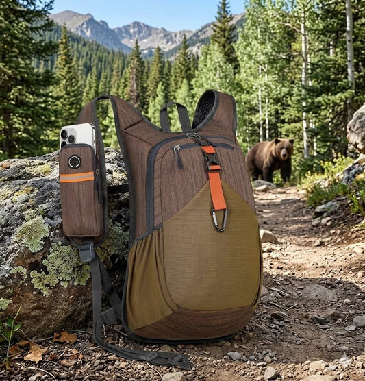 "Front view of 20L Chocolate Brown ultralight hiking daypack featuring orange accent strap and black carabiner in a mountain trail setting." Big Green Bear