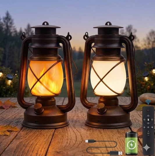 Two lantern-style outdoor lights with dark metal bodies and glowing warm light inside, placed on a wooden surface outdoors at dusk. A small remote control and charging cable/battery are shown at the lower right. big green bear