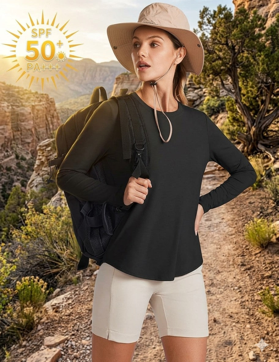 A woman hiking outdoors wearing a black long-sleeve performance top, beige shorts, a beige wide-brim hat, and carrying a dark backpack. An SPF 50+ sunscreen badge is visible in the top-left corner.