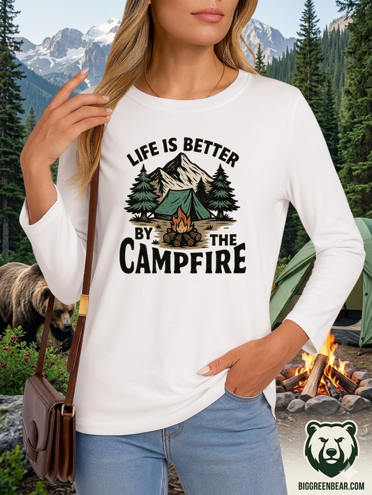 Person wearing a white long-sleeve shirt with 'Life is better by the campfire' design, standing in a camping setting. Biggreenbear.com